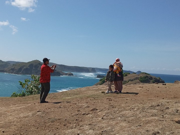 Wisatawan memotret keluarga di perbukitan dengan pemandangan laut biru Lombok Selatan