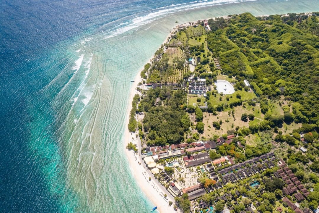 Garis pantai Gili Trawangan dengan air laut biru kehijauan dan vegetasi tropis.
