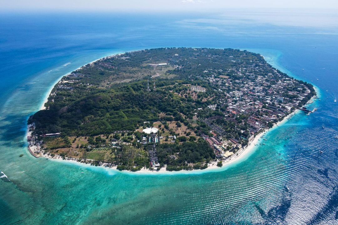 Pemandangan Gili Trawangan dengan garis pantai pasir putih dan laut biru kehijauan.